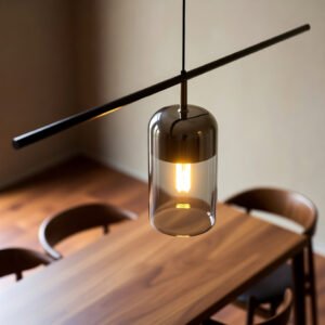 Pendente minimalista de vidro fumê com lâmpada de filamento LED, suspenso por haste metálica preta sobre mesa de jantar de madeira maciça.