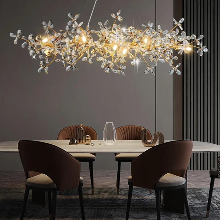 Lustre pendente horizontal de design orgânico com estrutura dourada e diversos cristais em formato de pétalas, iluminado sobre uma mesa de escritório e estante de livros cinza.